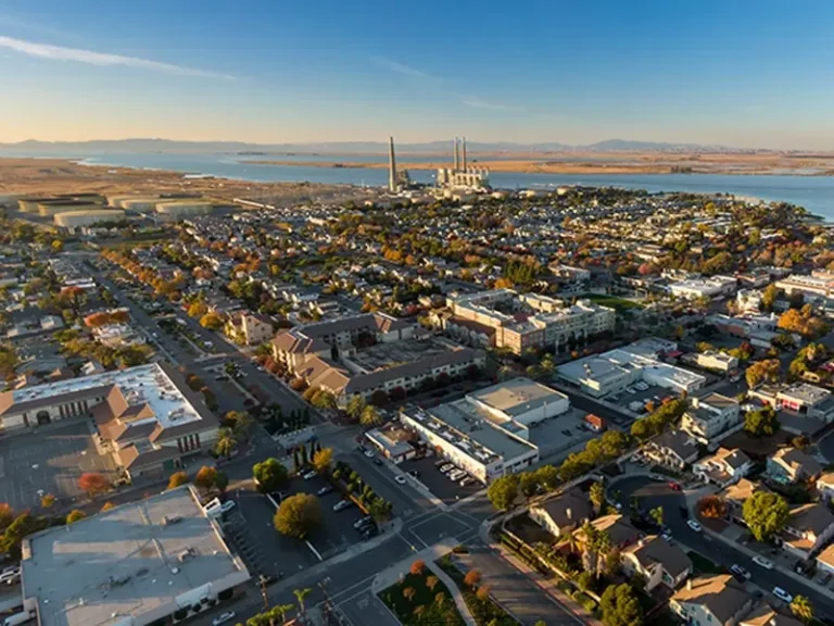 Aerial view of a suburban neighborhood with industrial buildings and a body of water in the background.