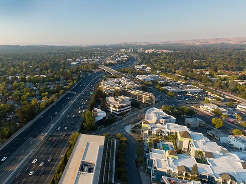 Aerial view of a highway running through a suburban area with buildings and trees on both sides.